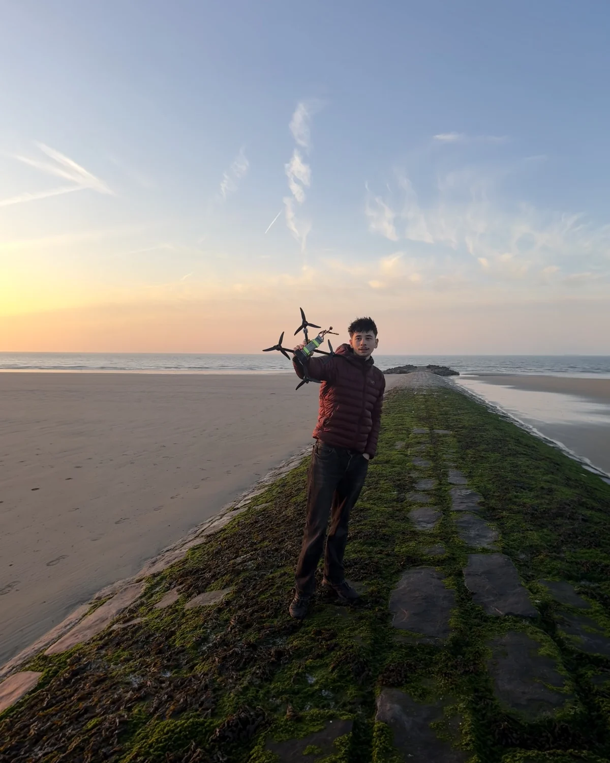 Maxime Palasthy aan de Belgische kust met zijn FPV-drone in de hand, bij zonsondergang